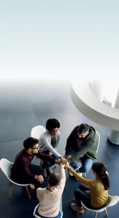 Group of people sitting in a circle with hands together on a light background