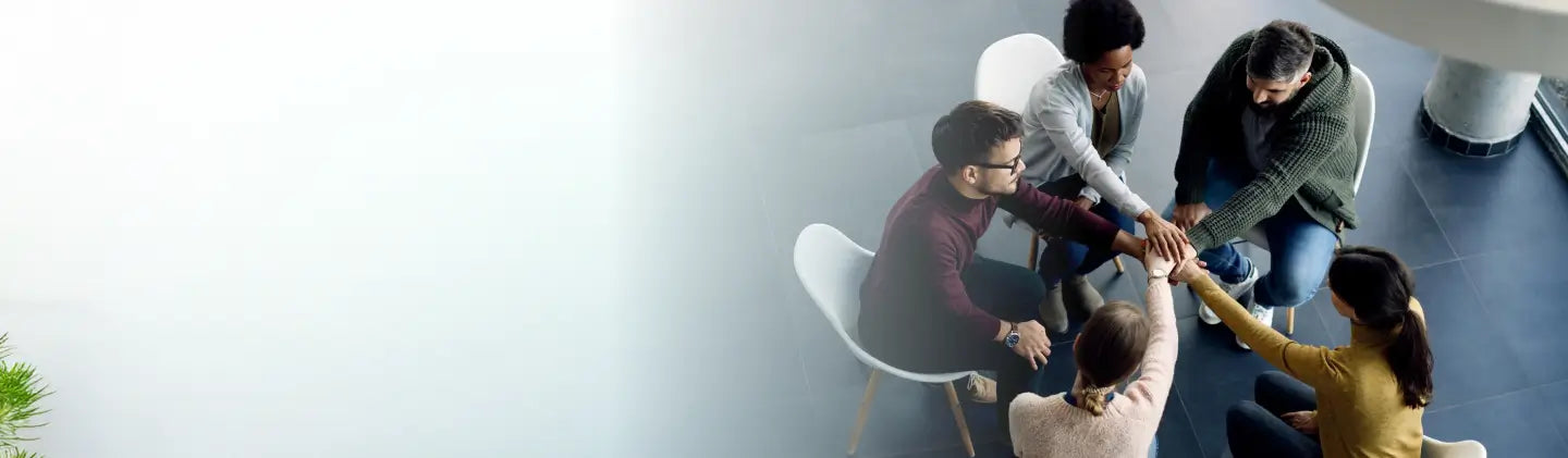 Group of people sitting in a circle with hands together on a light background