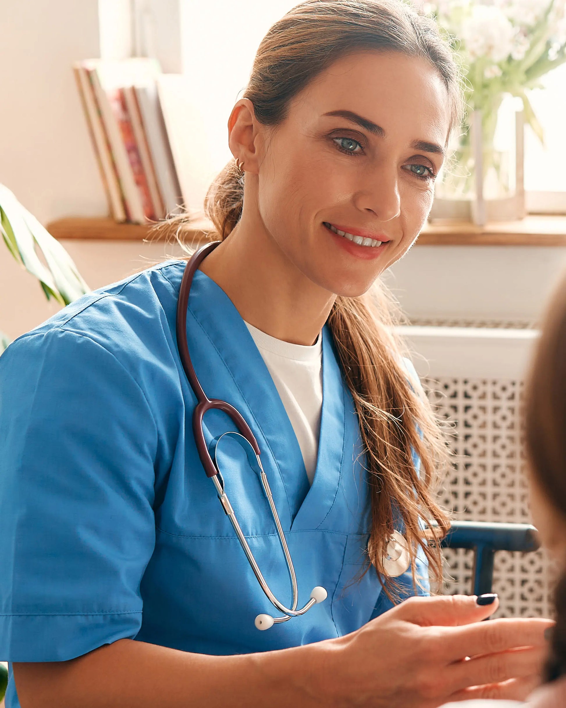 Nurse in blue scrubs with a stethoscope, smiling at a patient.